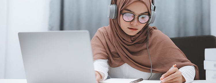 Woman with headphones and laptop learning online completing virtual classes and training.