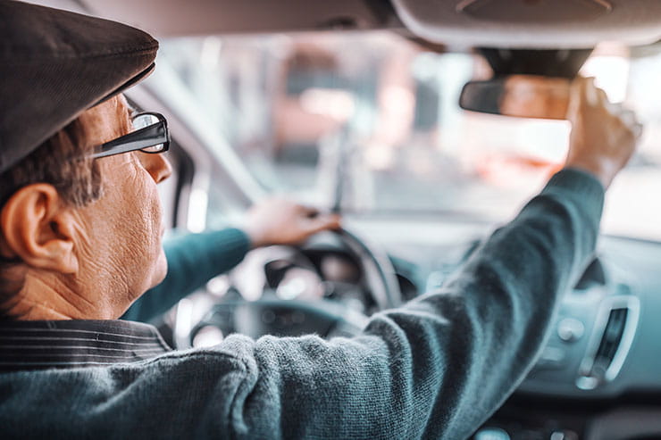 Best jobs for seniors over 60: Senior man with hat and eyeglasses adjusting rear mirror while sitting in his car