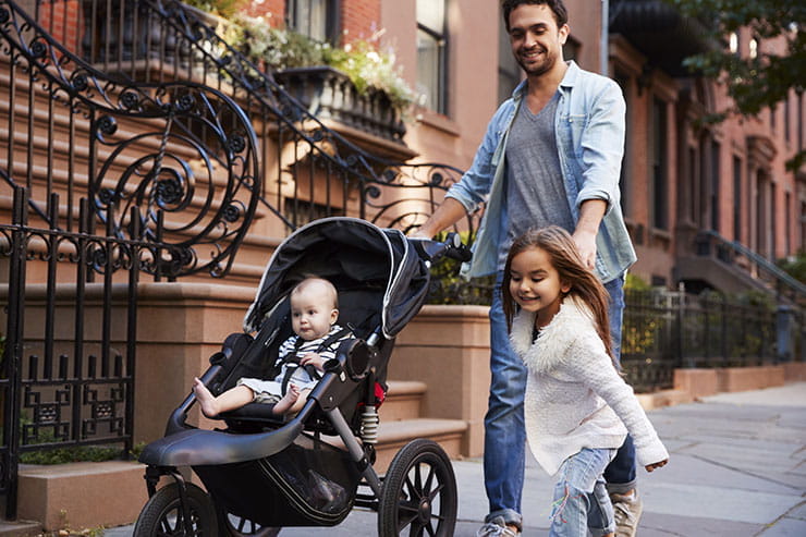 Father pushing baby in a stroller while holding daughter's hand